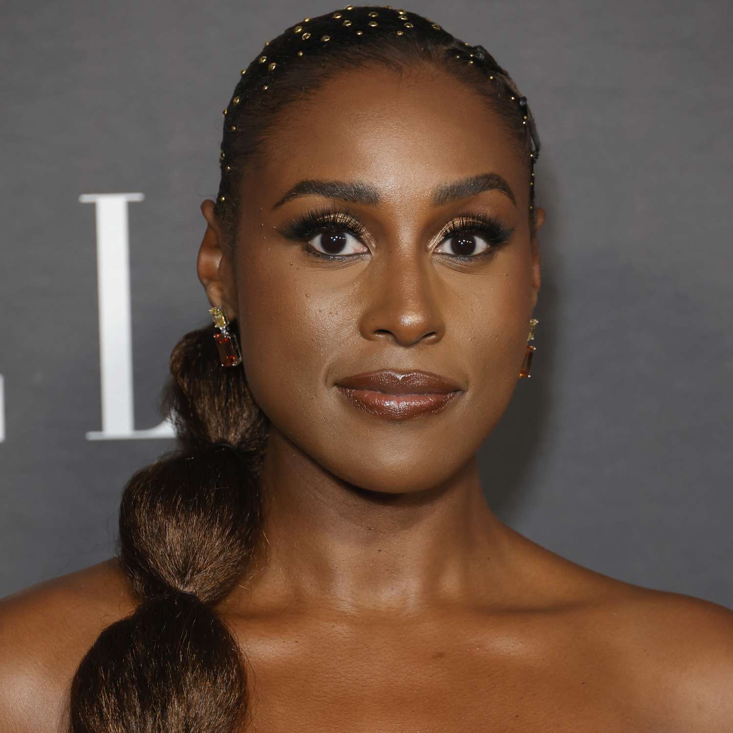 Issa Rae wears a low bubble ponytail with brass gem accents on her roots