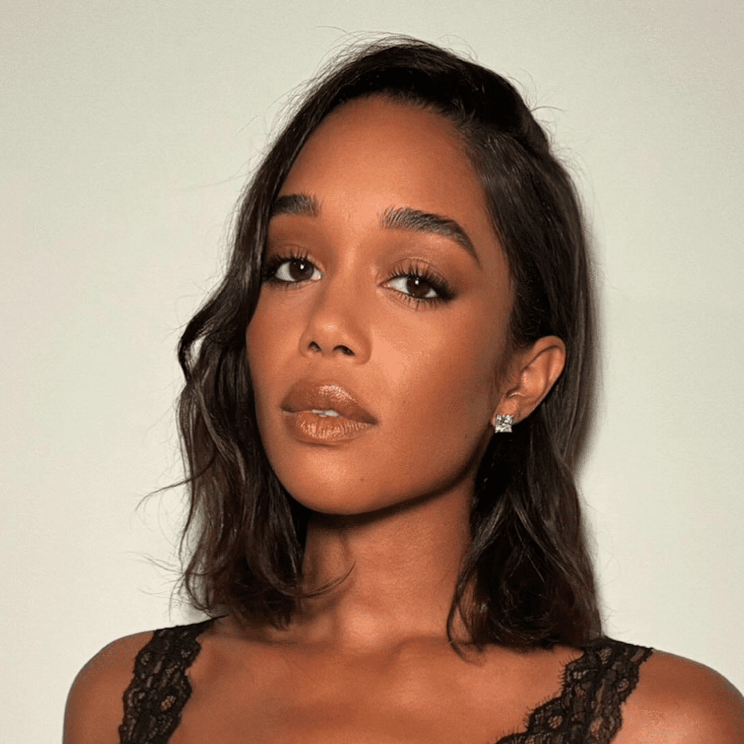 Laura Harrier wears her espresso brunette lob in undone tousled waves with a deep side part and thick, full brow