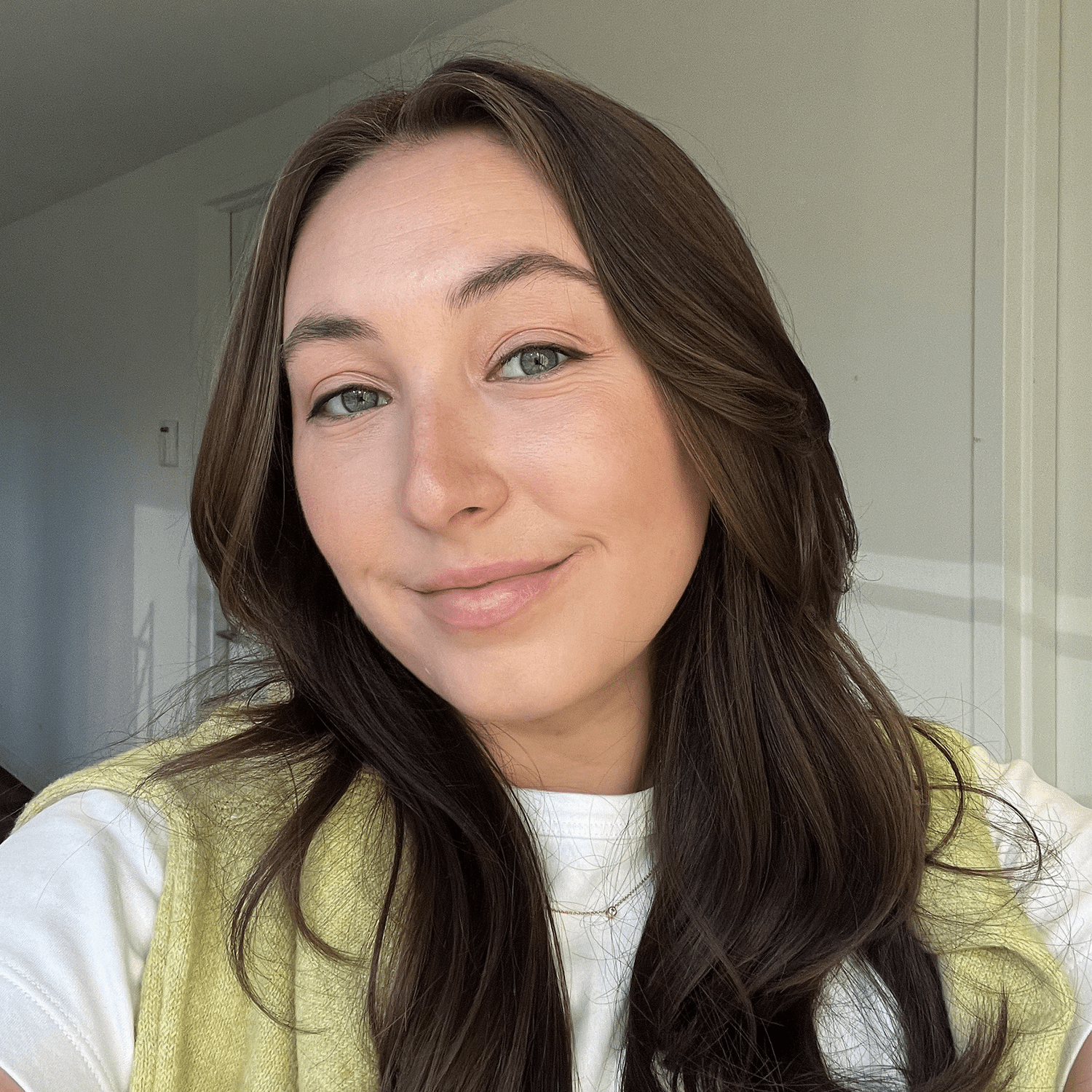 Woman with long brown hair wearing a white t shirt and green sweater