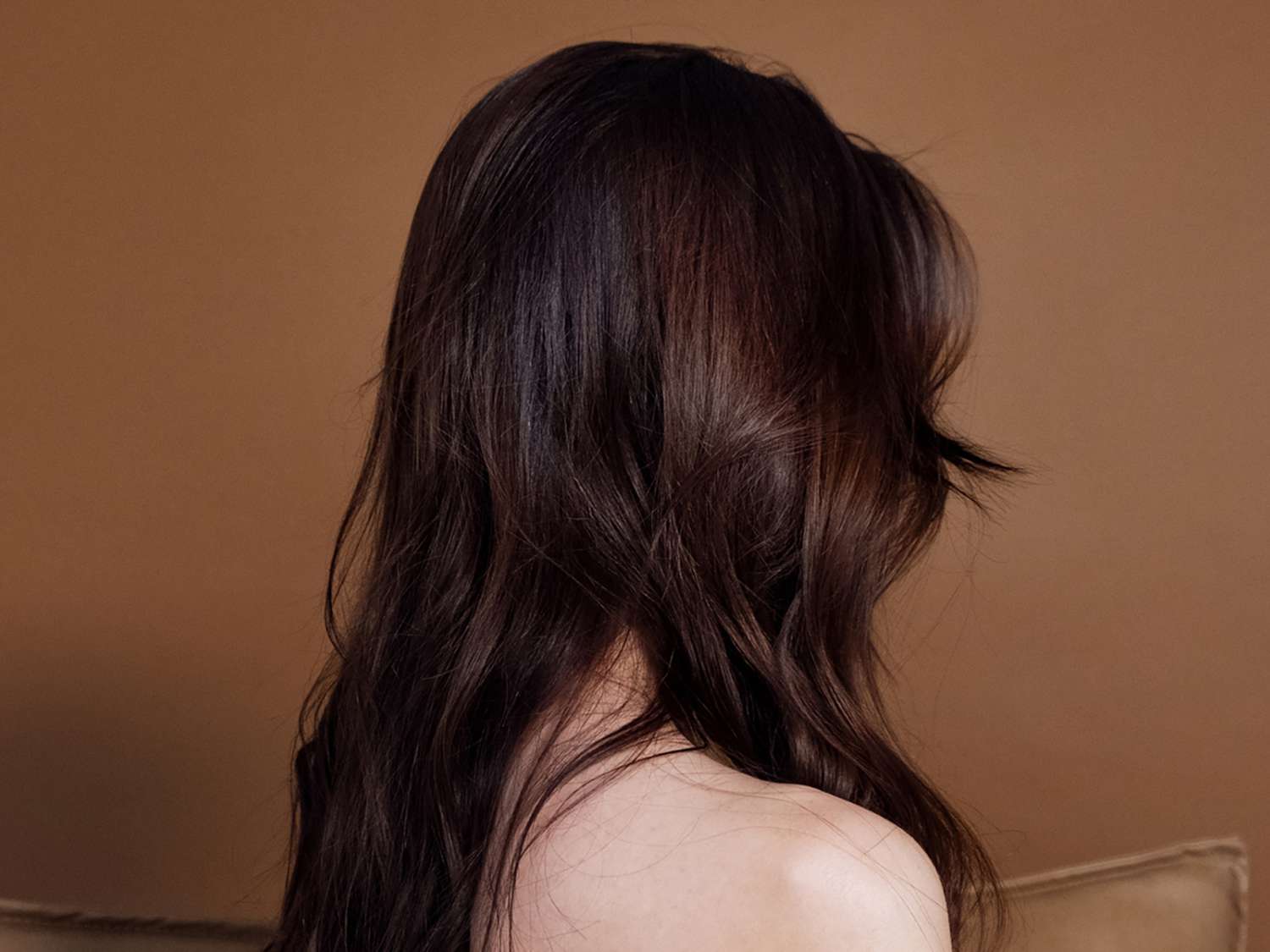 A woman with long, dark hair, covering her face, viewed from side profile. 